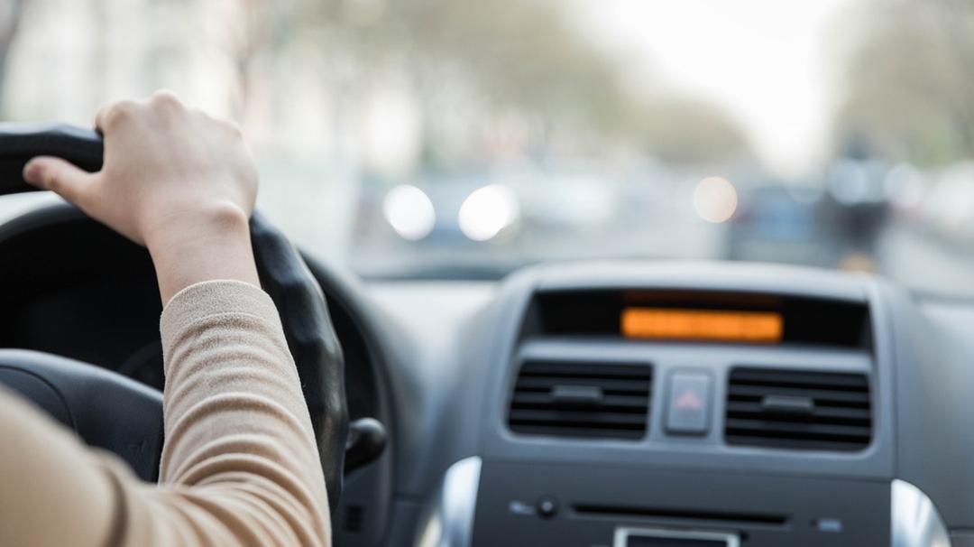 Woman's hand on a steering wheel, driving in traffic