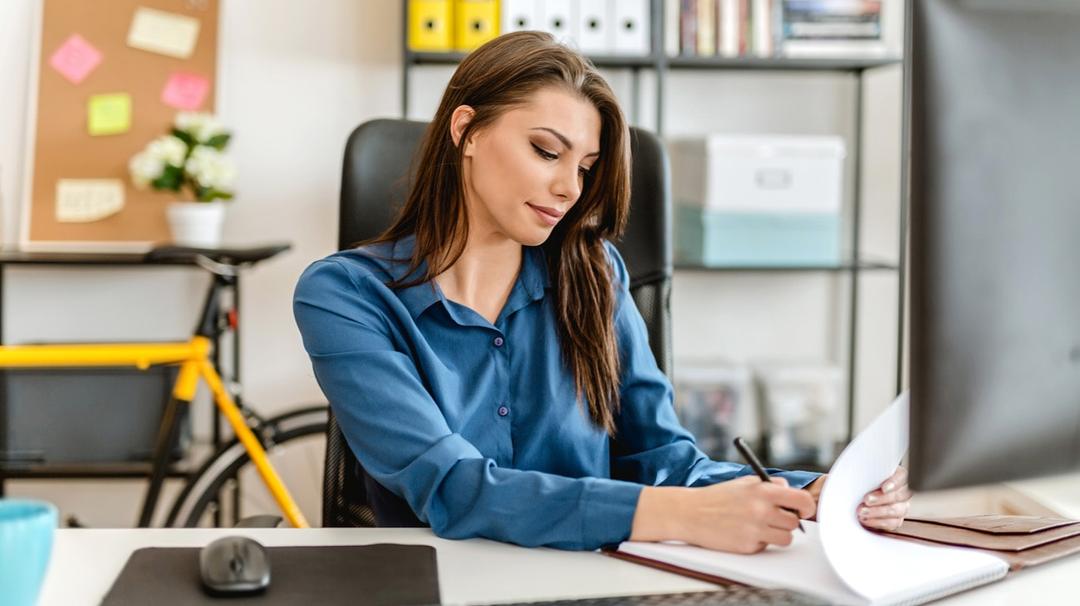 Business woman sitting at a desk, writing a business plan with pen and paper.