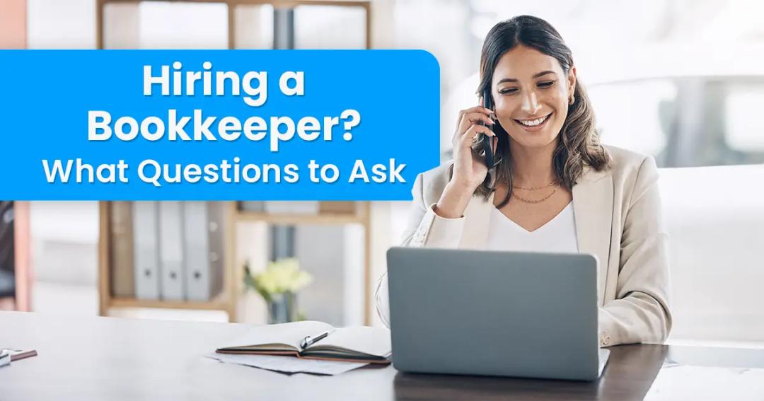 A person in business attire is sitting at a desk, talking on the phone, and using a laptop. Text beside them reads, "Hiring a Bookkeeper? What Questions to Ask.