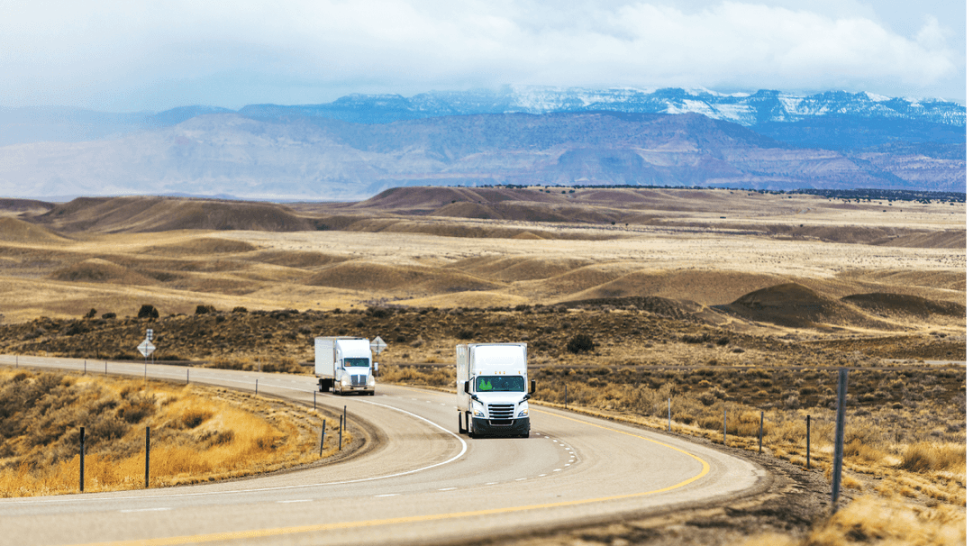 Two tractor trailers driving around a bend in the open plains.