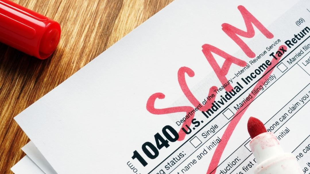A u.s. tax form 1040 stamped with "scam" in red ink, with a red marker lying next to it on a wooden surface.