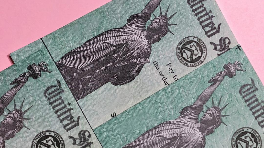 CARES Act stimulus checks laying on a pink background