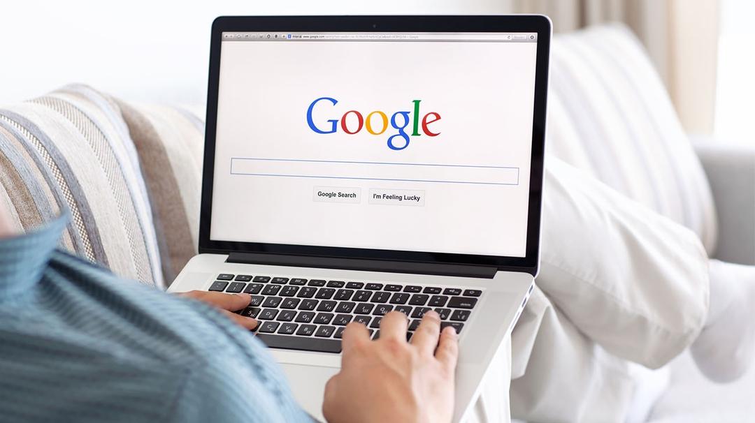 man holding a laptop on his lap looking at Google's home screen