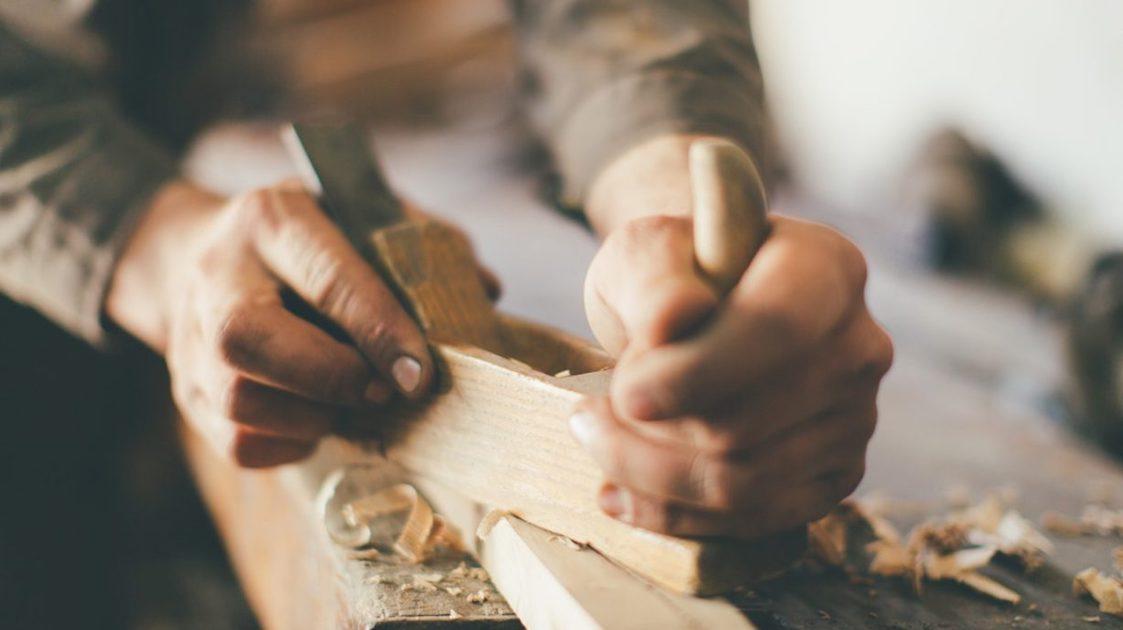 A pair of hands chiseling away at a wooden block