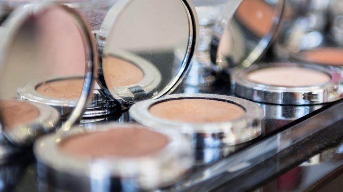Makeup powders in silver compacts in a line on a shelf