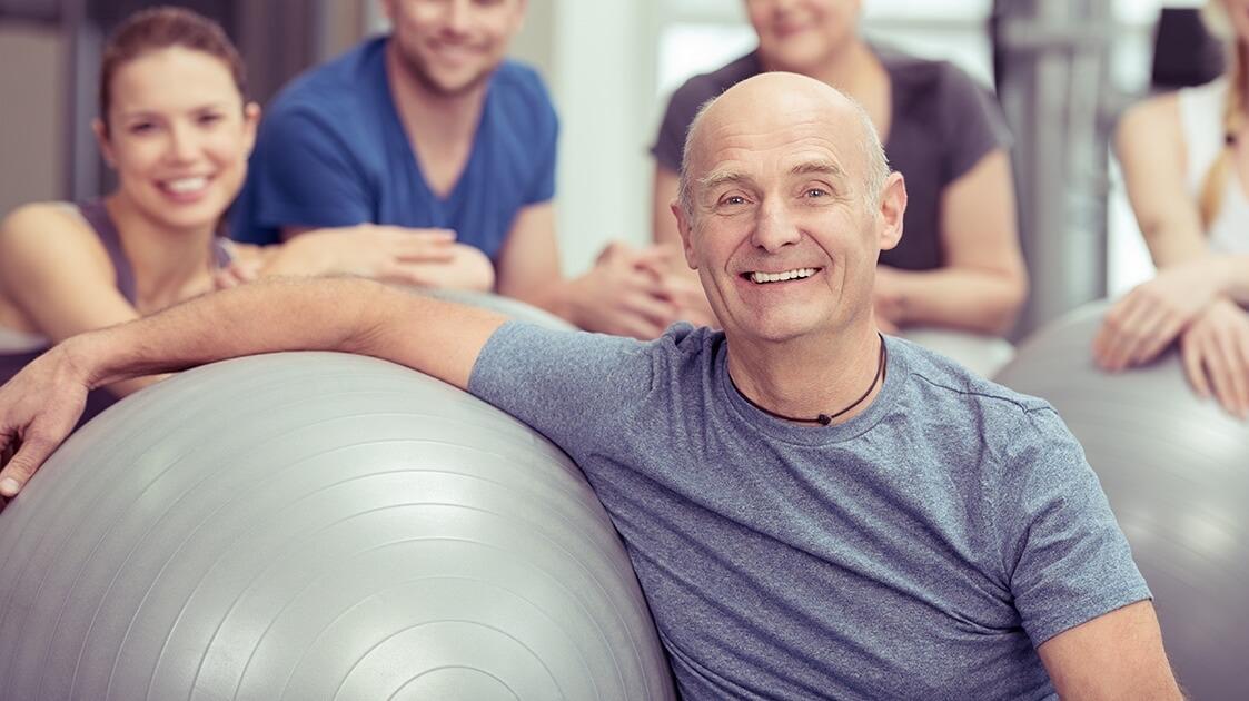 Man leaning against an exercise ball in front of three smiling people